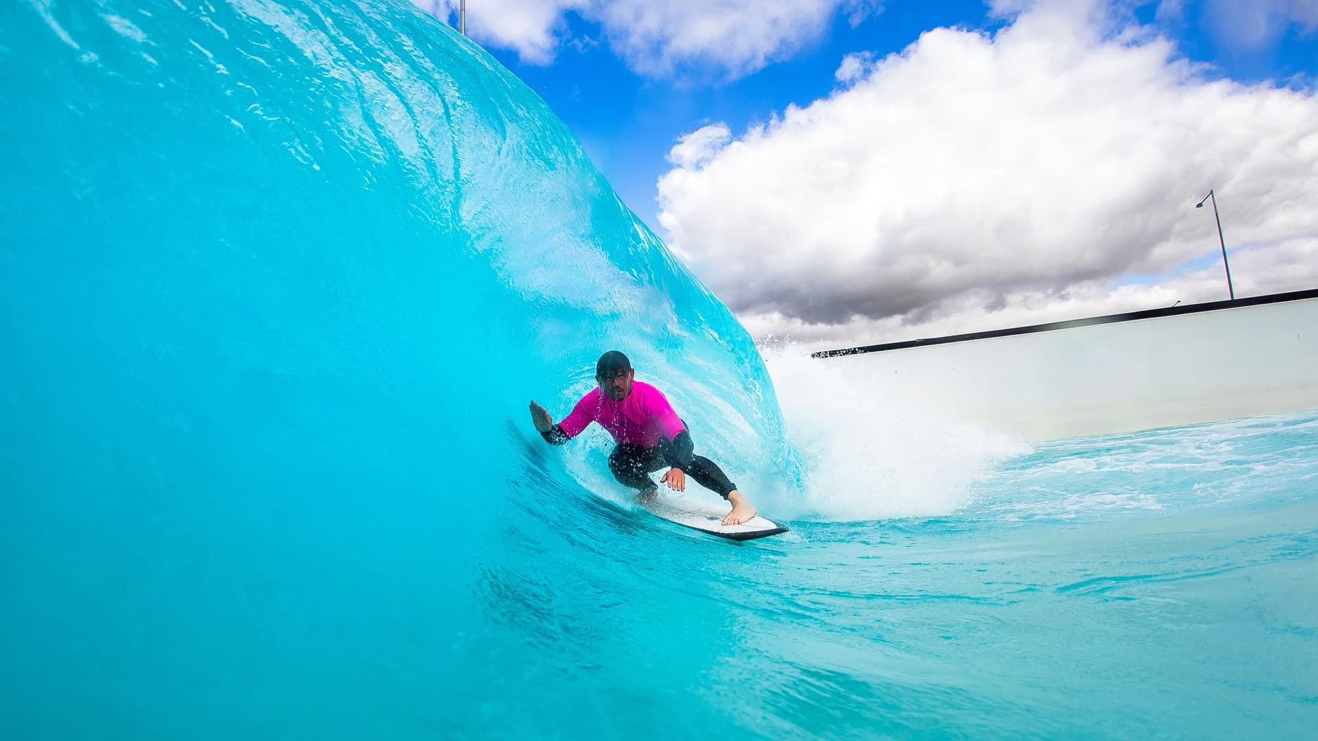 A surfer in a bright pink rash guard carving through the wall of a turquoise barrel wave.