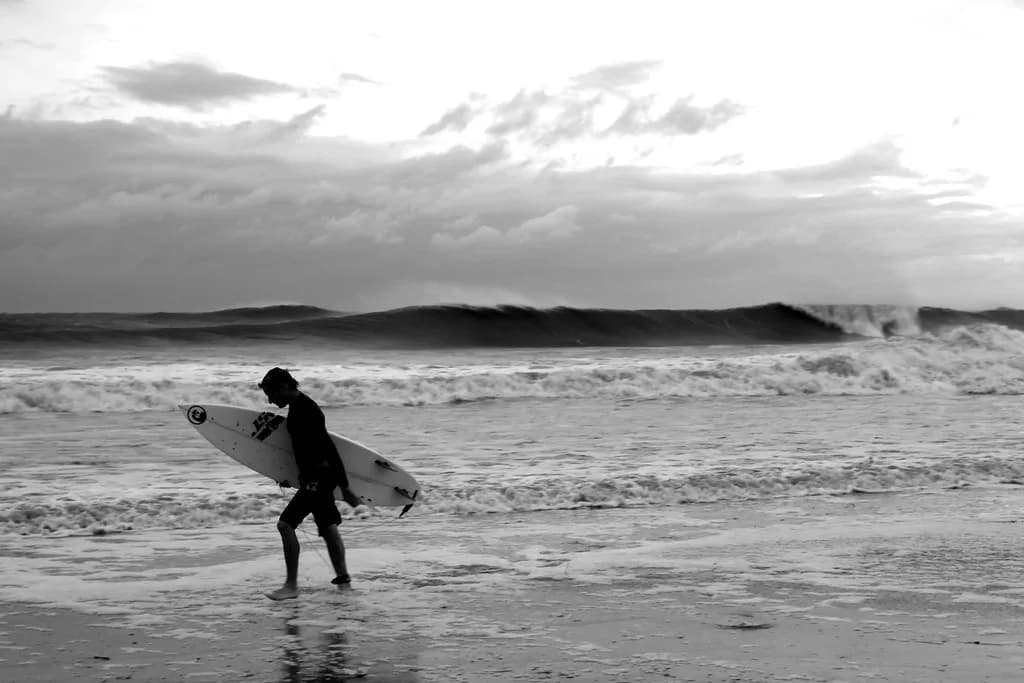 Surfer walking up the beach at Folly Beach, South Carolina, as Hurricane Irene swell breaks behind him