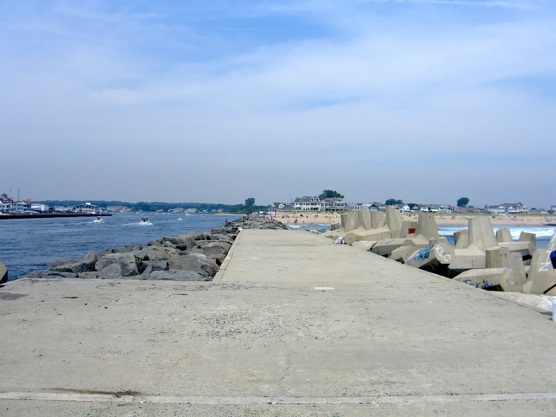 The Manasquan Inlet jetty on a summer day, with the beach and lineup beyond it