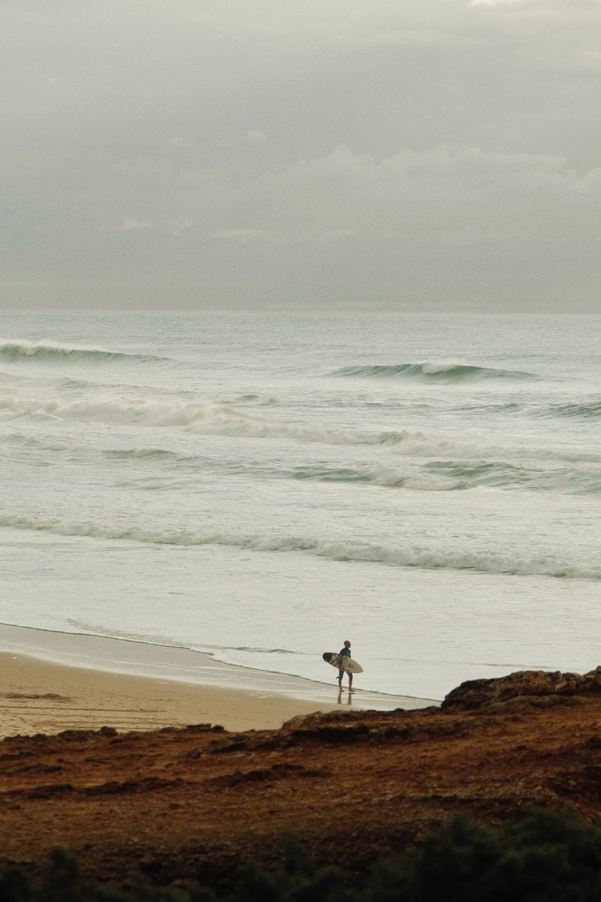 Surfer walking toward gentle waves at a beginner-friendly beach