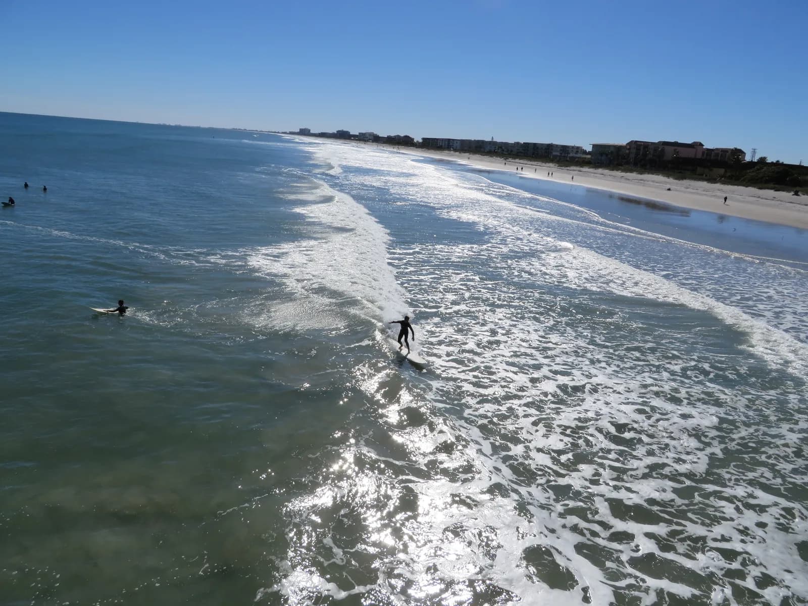 Surfers on small lined-up waves south of the Cocoa Beach Pier, seen from the pier deck