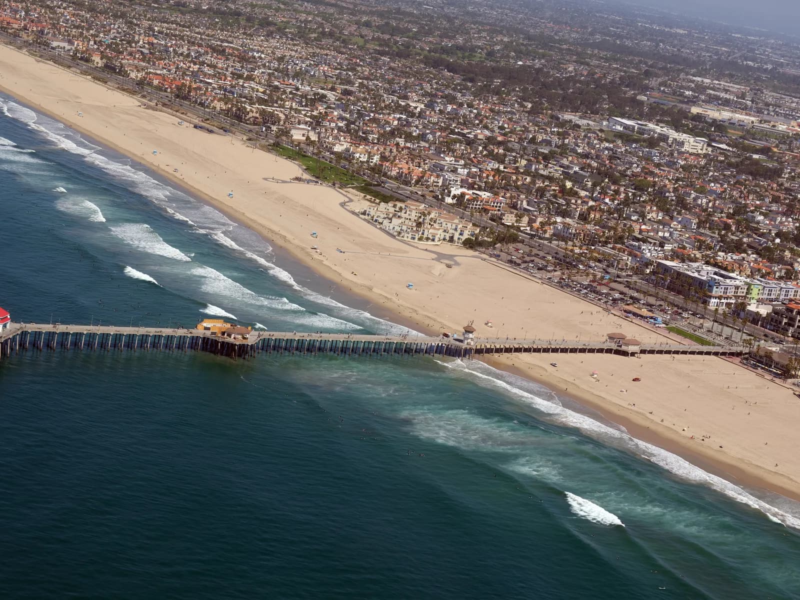 Aerial view of Huntington Beach Pier and the long straight beach with small lines of surf