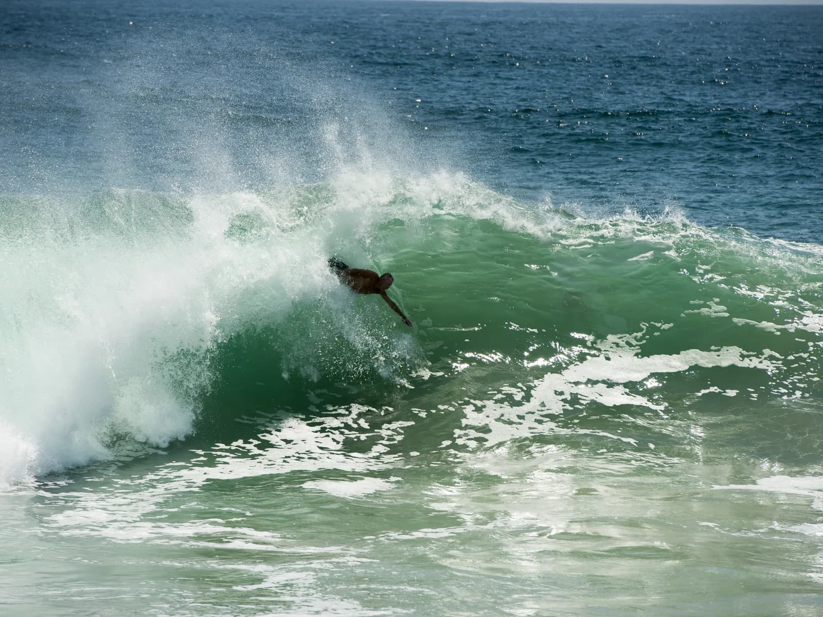 A thick green wave pitching at the Wedge with a rider in the lip